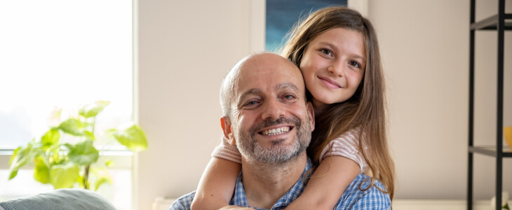 Young daughter hugging father from behind, both smiling