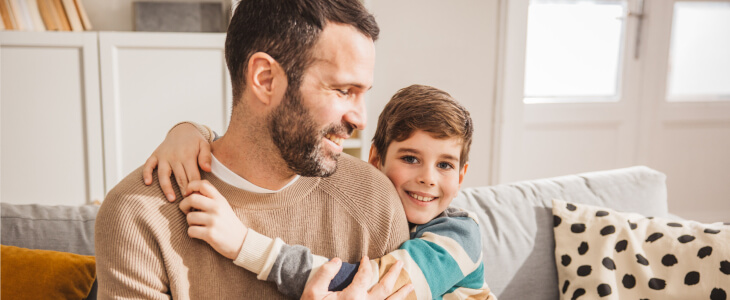 Young boy hugging father, both smiling