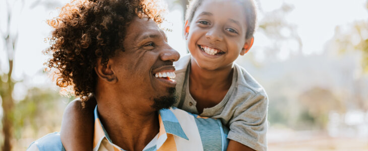 Father with son on his back, both smiling, outdoors