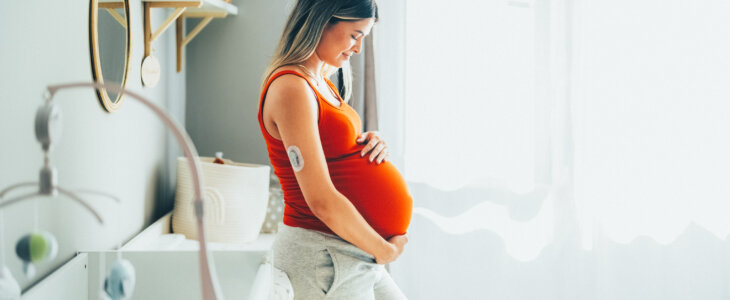 Young pregnant woman standing in nursery holding belly