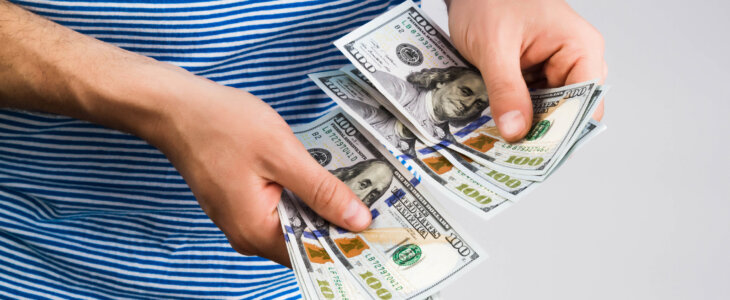 Man in a blue striped shirt holding several hundred dollar bills