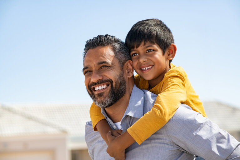 Happy middle eastern child enjoying ride on father's back outdoor.