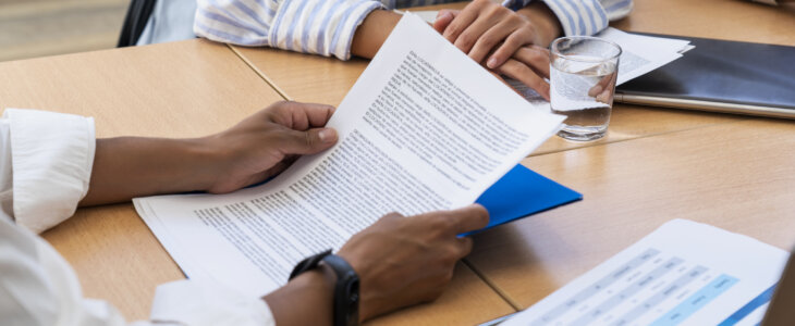 Close-up shot of hands holding papers on a table full of documents and computer